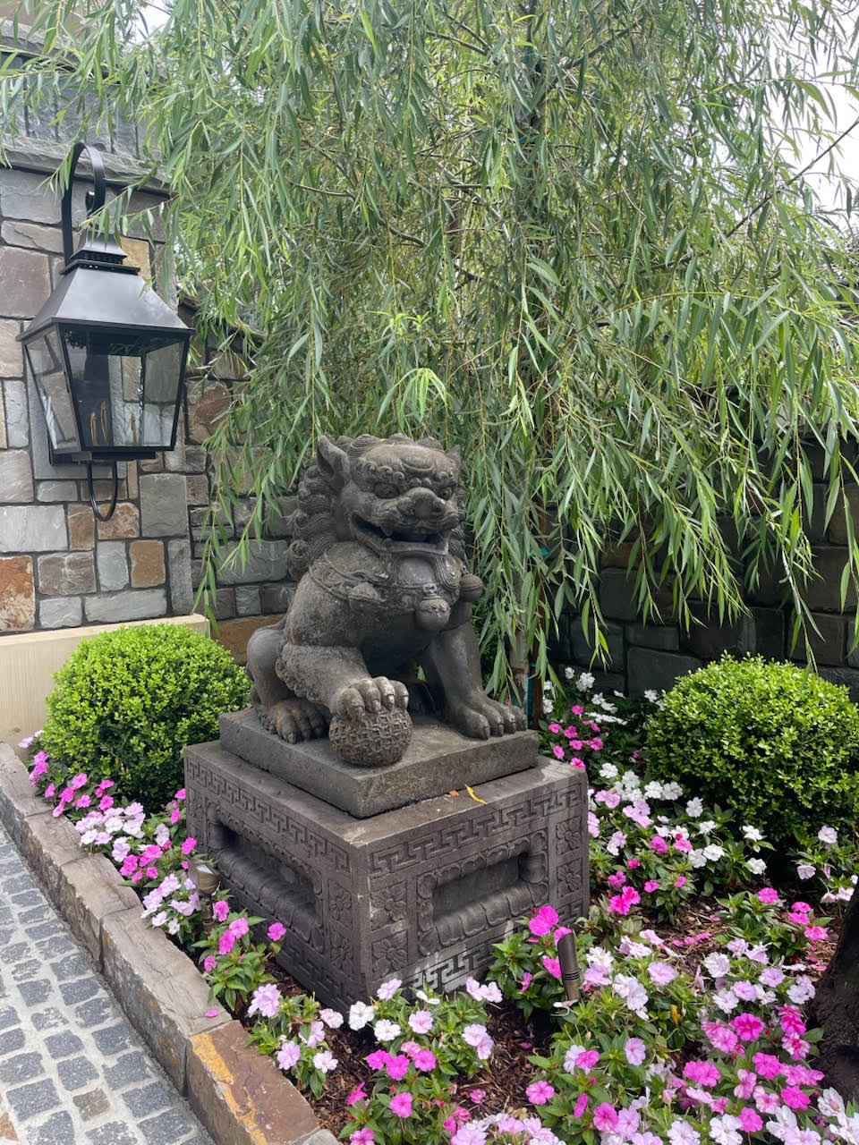 Carved guardian lion garden statue on a pedestal in a flower bed